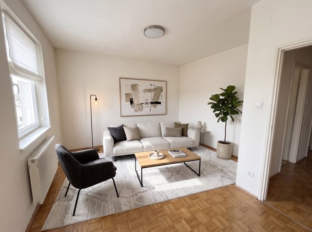 Nach Virtual Staging im Stil Modern: ein helles Sofa, ein dunkler Sessel, ein Couchtisch aus Holz und Metall, ein heller Teppich, eine Stehlampe, abstrakte Kunst und eine Geigenfeige, mit einem Raffrollo aus Stoff am Fenster und einer neuen flachen Deckenleuchte