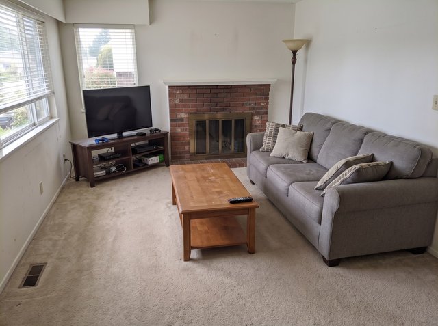 After, attempt 2: the same living room with the same sofa, coffee table, TV console, floor lamp and fireplace, but no mail, laundry, backpack, shoes, photos or drawings; a small boxed item now sits on the lower console shelf