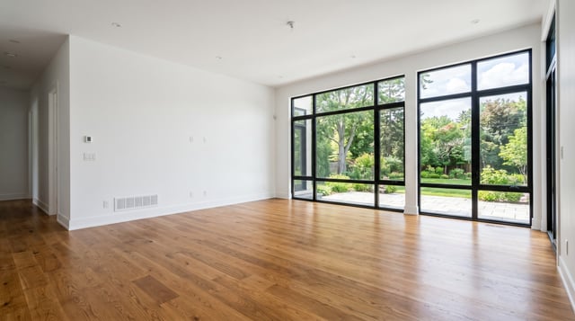 Before: empty living room with white walls, oak floor and floor-to-ceiling black-framed windows onto a garden