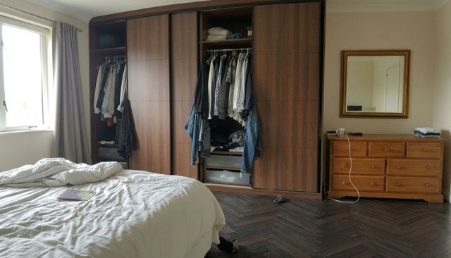 After: the same bedroom with a dark herringbone wood floor running in perspective under the bed and chest of drawers