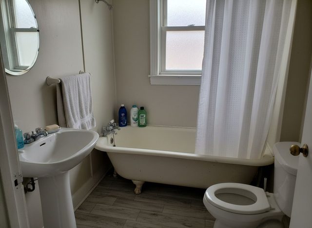 Before: small bathroom with gray wood-look plank flooring, a clawfoot tub, a pedestal sink and a toilet