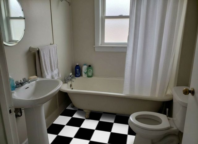 After: the same bathroom with a black and white checkerboard tile floor running under the clawfoot tub and around the toilet, with the fixtures unchanged